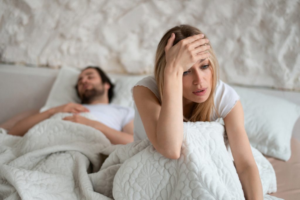 unhappy woman sitting on bed, suffering from her boyfriend's snoring, feeling dissatisfied because of sexual problems